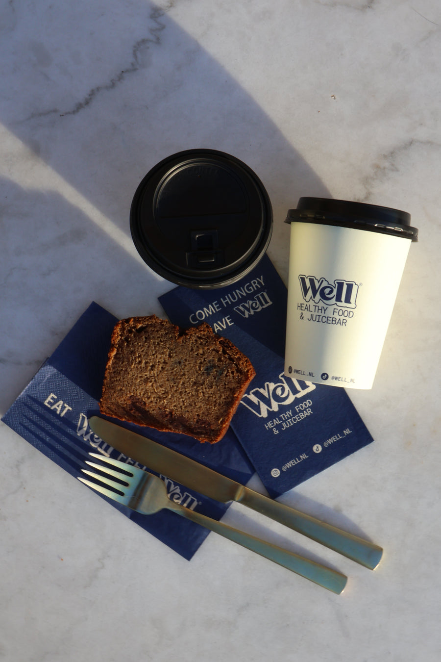 Bedrukte koffiebeker en servetten van Well naast een plak cake